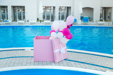 The pink box is a surprise against the backdrop of a pool with helium balloons.