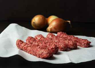 Raw kebab on white paper, onion on dark background