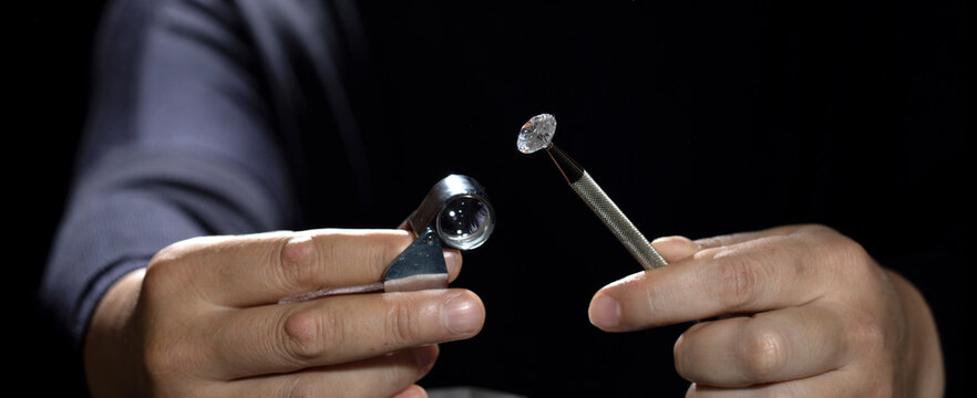 Close up of asian male diamond dealer buyer expert evaluates polished diamonds at exhibition. High quality photo