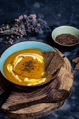 Vegetarian pumpkin soup with cream, flax-seeds and bread on dark background