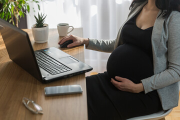 Pregnant woman is working on computer laptop and mobile phone, business. Being pregnant at work. ...