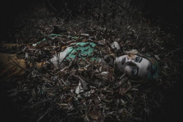 dead girl in autumn foliage wearing green and yellow robes