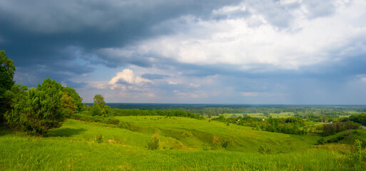 Fototapeta na wymiar wide green hills under a dense cloudy sky, summer rural scene