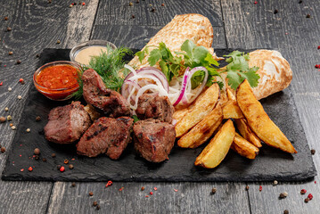 Juicy beef shish kebab with sauce, potatoes, pita bread and herbs