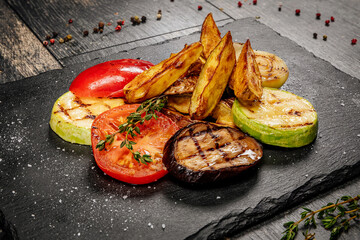 Juicy grilled vegetables: tomato, eggplant, zucchini, potatoes. served on a black hot stone