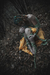 dead girl in autumn foliage wearing green and yellow robes