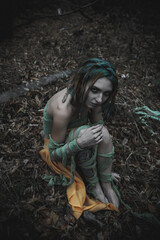 dead girl in autumn foliage wearing green and yellow robes