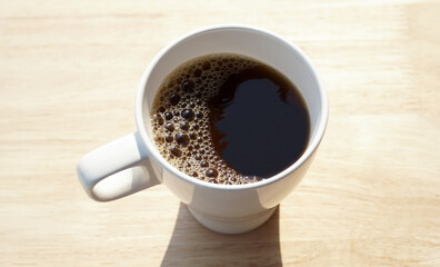 White cup of black coffee and spoon isolated on wooden background