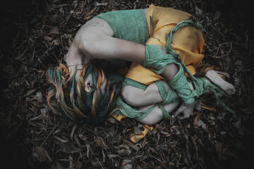 dead girl in autumn foliage wearing green and yellow robes