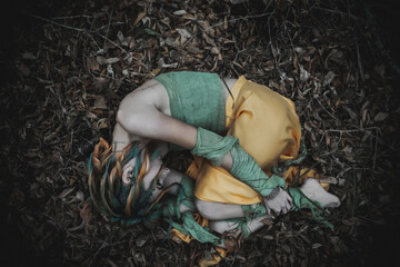 dead girl in autumn foliage wearing green and yellow robes
