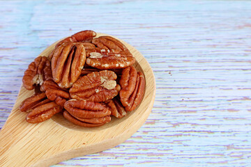 Closeup Heap of Pecan Nuts on a Wooden Spoon Isolated on Pale Blue Wooden Background