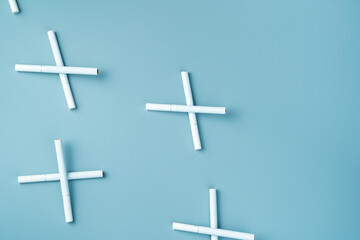 The cigarettes are laid out in the form of crosses on a blue background. Top view, horizontal, with space to copy. The concept of the dangers of smoking.