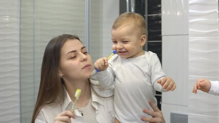 Smiling mother and son baby boy brushing their teeth together with toothbrush. Mom teaching cute child how to brush teeth