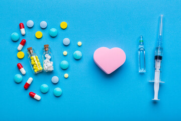 A lot of pills and syringe with injection on blue background with a heart shape as a symbol of medical treatment. Choice antibiotics against vaccine from Covid-19. Emergency help if a heart attack hap