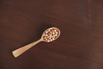 Raw chickpeas in a wooden spoon on a wooden background. Top view. Copy, empty space for text