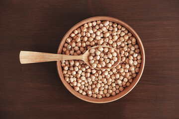 Dry chickpeas in a wooden plate and spoon on a brown wooden background. Top view. Copy, empty space for text