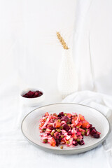 Russian traditional salad with vegetables - vinaigrette on a plate and a bowl of beets on a table on a cloth. Vertical view