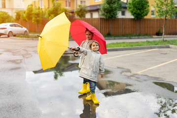 Children play with umbrellas after the rain in the street, run through puddles, have fun and play