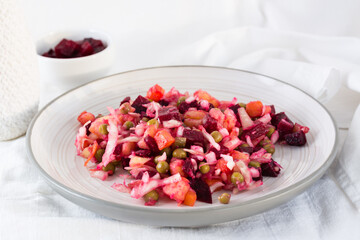 Russian traditional salad with vegetables - vinaigrette on a plate and a bowl of beets on a table...