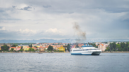 Passenger ferry entering Zadar bay from Adriatic Sea. Cruise ship mooring in harbour with urban and...