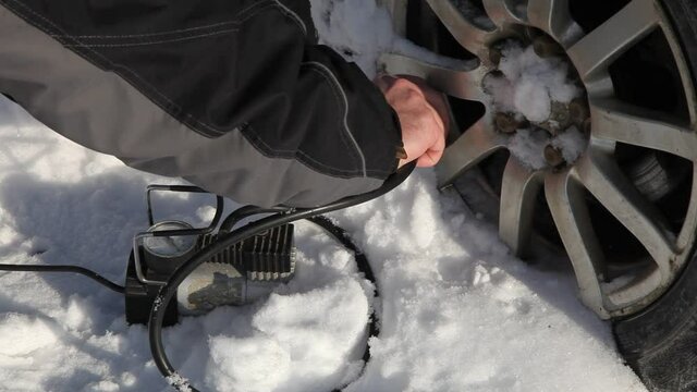 Man hand inflates with tire inflator hose portable electric air compressor the car wheel on white snow background at Sunny winter day, vehicle tyres pressure control, tyres self-repair