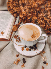 A white porcelain coffee cup with a saucer on a table with a beige tablecloth and an open book. The atmosphere of comfort. Cappuccino in an elegant cup.