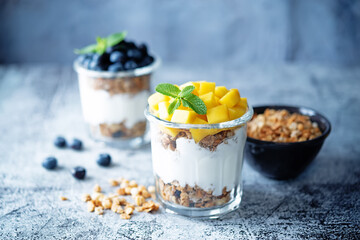 Mango  and blueberry Greek yogurt granola parfait in a glass