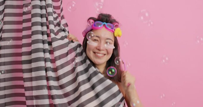 Good looking cheerful energetic young Asian woman dances happily while brushing teeth and taking shower shakes hands enjoys hygienic procedures has upbeat mood feels refreshed. Skin care concept