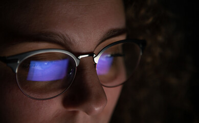 Computer screen reflected in the glasses of a woman who is working at night.