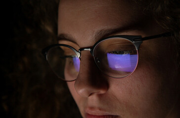 Reflection of a computer screen in glasses of a woman who is working at night.