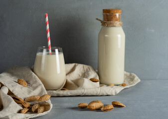Almond milk in a glass glass with a straw and in a small glass bottle. In the foreground, unpeeled almonds. Horizontal orientation
