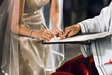A bride signs her wedding contract on the altar of a church with a priest.
