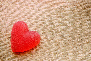 one red gummy candy in the form of a heart lies on the texture of the fabric of the bag close-up, orange background.