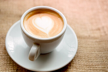 .one white cup on a saucer with a drink. coffee with milk, with foam heart stands on a windowsill...