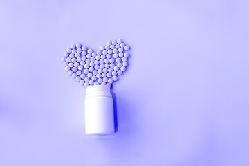 many small pills spilled out of a white jar on a purple background in the shape of a heart.