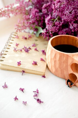 Wooden finnish cup with coffee on the table. Nearby lies a closed notebook for notes and a bouquet of lilacs. Good morning and good mood, planning a day at breakfast, concept.