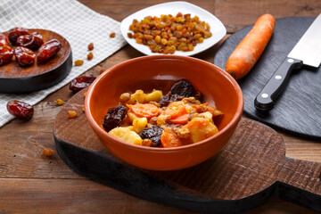 Jewish cuisine dish sweet tsimes with carrot dates vegetarian in a clay plate on a wooden board near candied fruits.