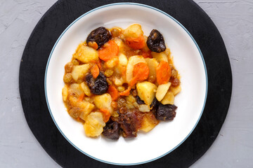 A dish of Jewish cuisine sweet tsimes with carrots and dates vegetarian in a plate on a round stand on a concrete background.