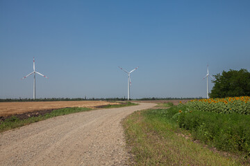 wind turbines on the background of a cloudy blue sky, view from a country road and sunflower fields