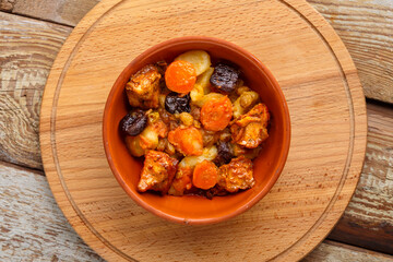 A dish of Jewish cuisine tsimes with carrots, dates and turkey meat in a clay plate on a wooden round stand top view.