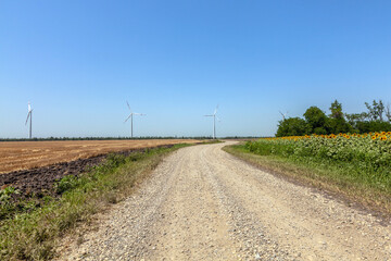 Fototapeta na wymiar wind turbines on the background of a cloudy blue sky, view from a country road and sunflower fields