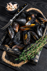 Steamed Mussels in shells in a wooden tray with herbs. Black wooden background. Top view