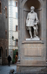 Fototapeta premium Florence, Italy - 2021, January 31: A view of the city, near the Uffizi museum courtyard. Benvenuto Cellini statue in the foreground. A man walking down the street.