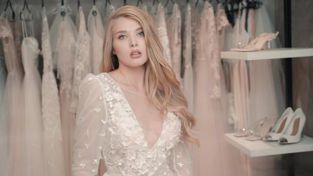 Portrait of woman in wedding dress looking at camera in store boutique. Seductive look of blonde