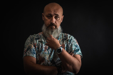 bald, bearded, man in a T-shirt. He straightens, straightens his beard and looks at you, posing on a dark background. Fashion and style. Close up, copy space 
