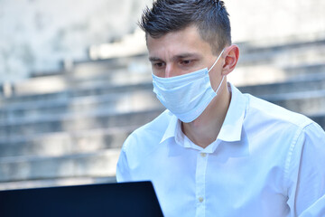 Businessman in mask working outdoor on laptop computer.