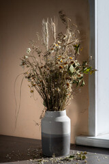 dried bent and floral composition that placed in a large vase stands on a table sunlit
