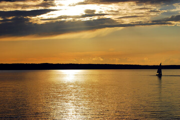 Fototapeta na wymiar Lone sailboat bathed in golden sunlight during sunset