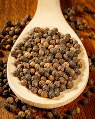 heap of black pepper on a spoon and wooden board