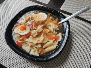 a plate of vegetable soup with butterflies pasta on the kitchen table
